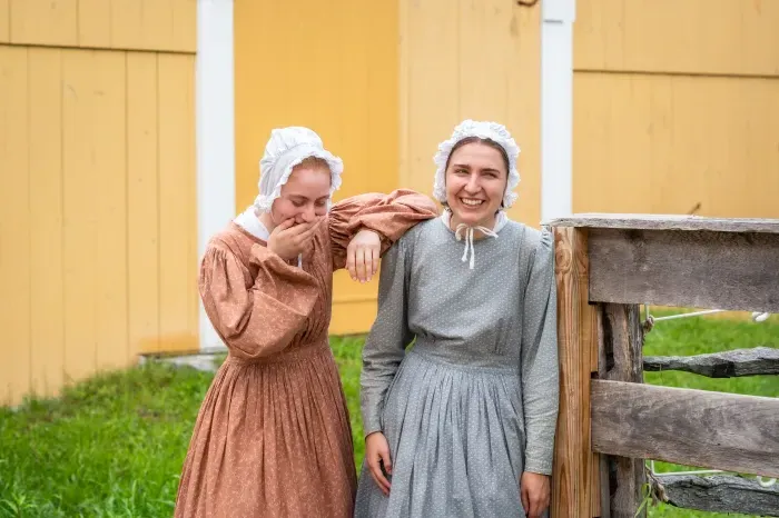 Two students, interns at a historical living museum, dressed in bonnets.