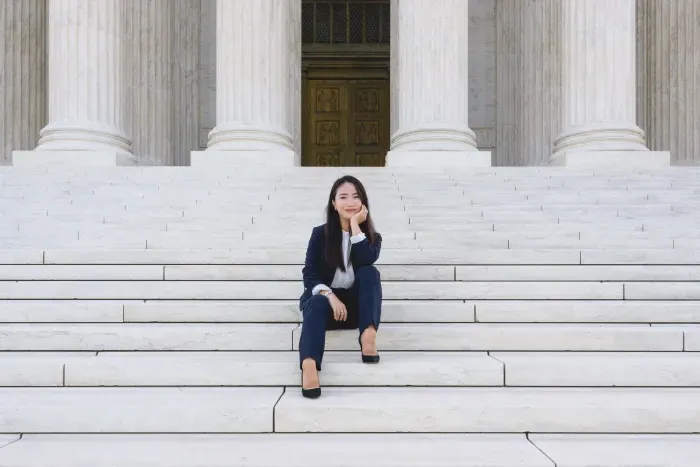 A student sitting on the steps of the Supreme Court in a suit.